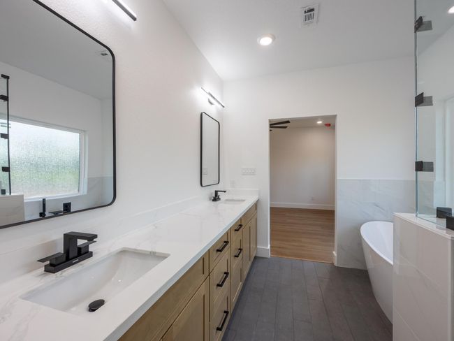Backlit mirrors, quartz countertops, and modern matte black fixtures complement the custom cabinetry for a sophisticated and functional primary bath. | Image 27