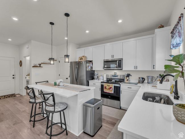 Kitchen with stainless steel appliances, a sink, a center island, a breakfast bar, and light wood-type flooring | Image 9