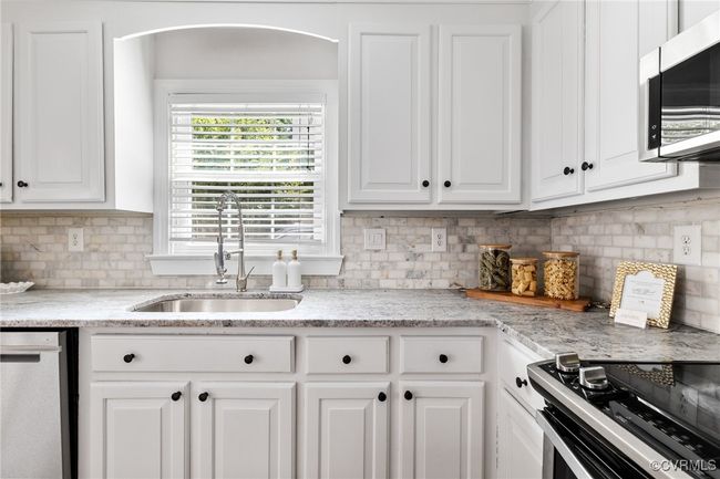 Kitchen with stainless steel appliances, new leathered granite, large ss sink beneath a window, white cabinetry, and tasteful backsplash. | Image 13