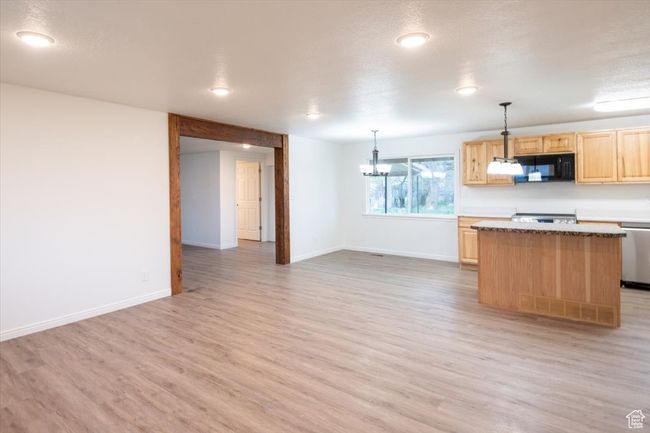 Kitchen featuring black microwave, light brown cabinets, a center island, baseboards, and light wood-type flooring | Image 13