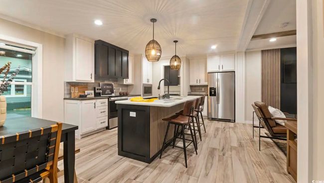 Kitchen featuring appliances with stainless steel finishes, tasteful backsplash, a center island with sink, light wood-style floors, and white cabinets | Image 18