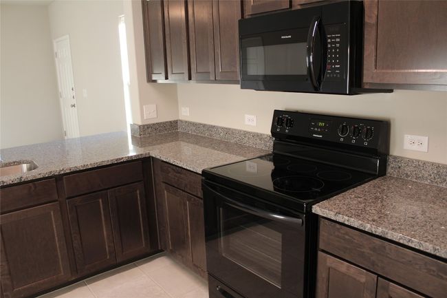 Kitchen featuring black appliances, dark brown cabinets, light stone countertops, and light tile patterned floors | Image 8