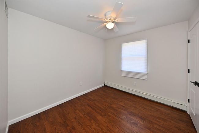 Unfurnished room featuring dark wood-type flooring, ceiling fan, baseboards, and a baseboard radiator | Image 10