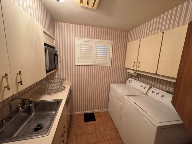 Washroom featuring wallpapered walls, cabinet space, separate washer and dryer, light tile patterned floors, and baseboards | Image 38