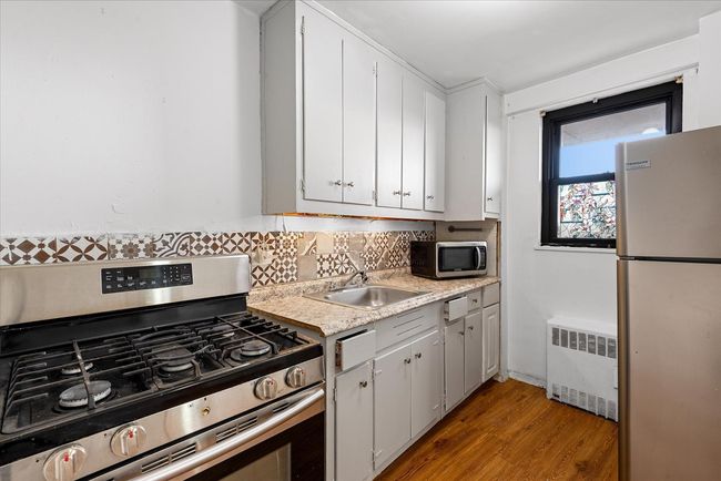 Kitchen with radiator heating unit, a sink, light countertops, backsplash, and appliances with stainless steel finishes | Image 8