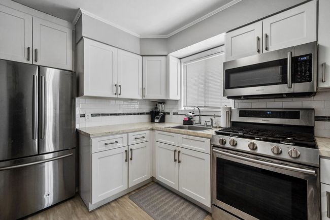 Kitchen featuring light wood finished floors, backsplash, a sink, crown molding, and appliances with stainless steel finishes | Image 7