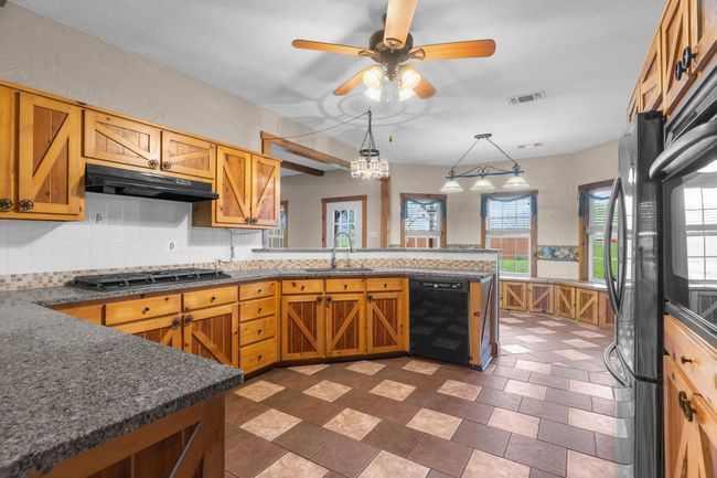 Kitchen with visible vents, black dishwasher, a peninsula, under cabinet range hood, and stainless steel gas stovetop | Image 16