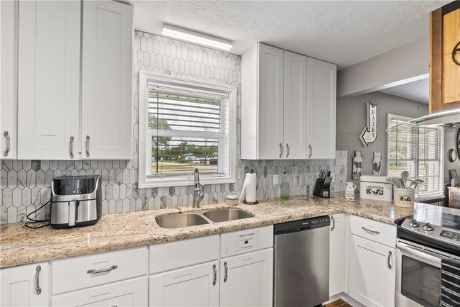 Kitchen featuring appliances with stainless steel finishes, white cabinetry, decorative backsplash, and a textured ceiling | Image 13
