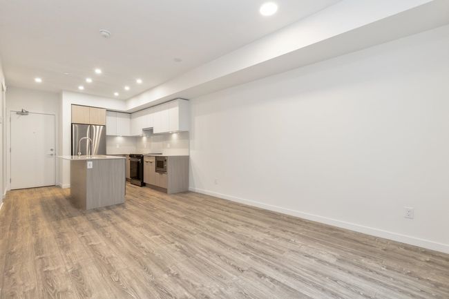 Kitchen featuring freestanding refrigerator, light wood-type flooring, an island with sink, open floor plan, and recessed lighting | Image 6