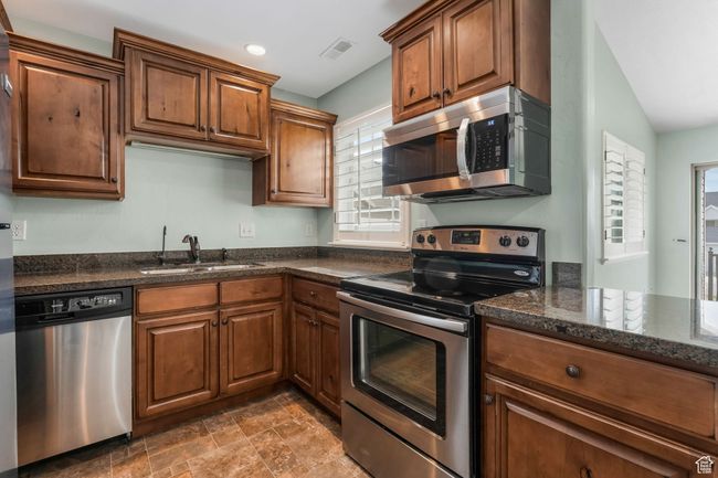 Kitchen featuring dark stone countertops, a sink, visible vents, appliances with stainless steel finishes, and brown cabinetry | Image 6