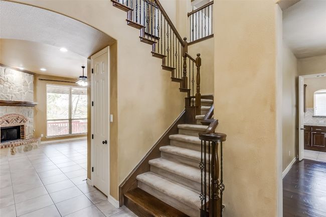 A beautiful staircase, a cozy fireplace, tile patterned flooring, baseboards, arched walkways, and ceiling fan | Image 6