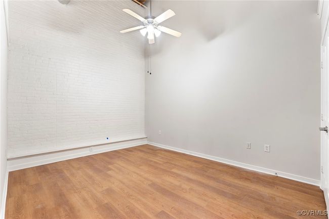 Spare room featuring a ceiling fan, baseboards, wood finished floors, and brick wall | Image 10