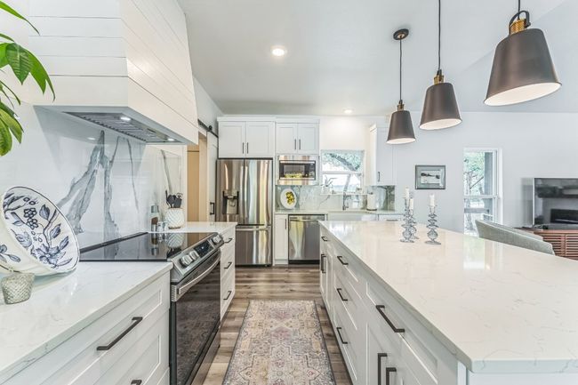 Stainless steel appliances, wood finished floors, white cabinetry, decorative backsplash, and light and beautiful countertops. | Image 9