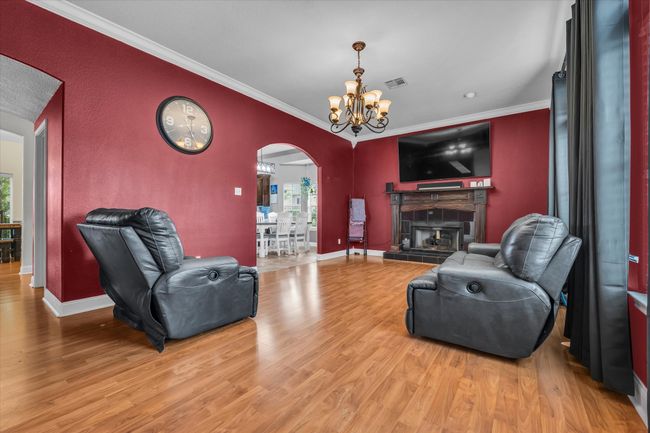 Living room featuring arched walkways, crown molding, light wood-style flooring, a chandelier, and a tiled fireplace | Image 11