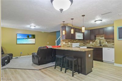 Kitchen with light colored carpet, a breakfast bar, backsplash, and white appliances | Image 3