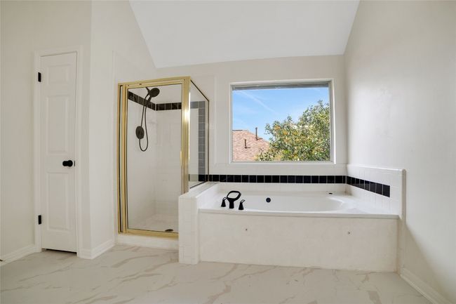 Bathroom featuring marble finish floors, a bath, a stall shower, vaulted ceiling, and baseboards | Image 24