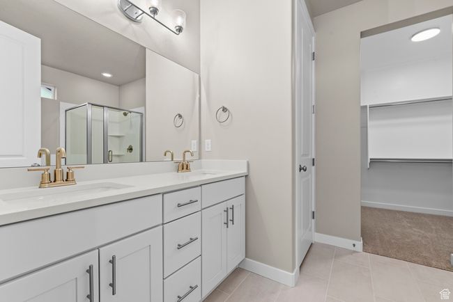 Full bathroom featuring double vanity, a shower stall, a walk in closet, baseboards, and tile patterned flooring | Image 15
