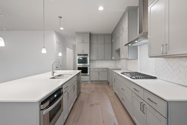 Kitchen featuring a sink, appliances with stainless steel finishes, gray cabinetry, light wood-type flooring, and wall chimney range hood | Image 12