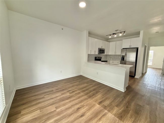 Kitchen featuring stainless steel appliances, a peninsula, tasteful backsplash, white cabinets, and light countertops | Image 20