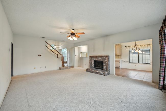 Unfurnished living room featuring light colored carpet, a ceiling fan, stairway, a brick fireplace, and a chandelier | Image 12