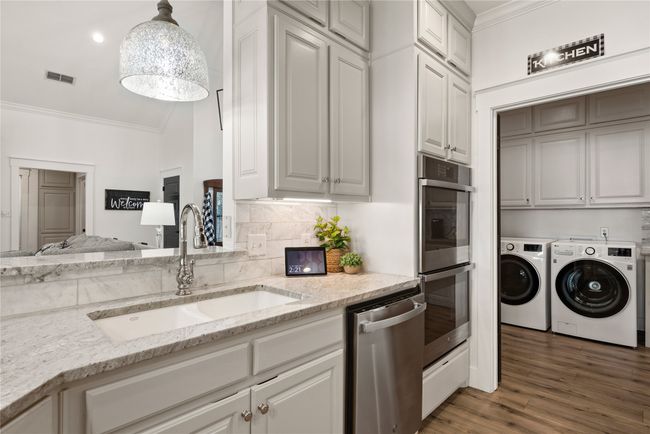 Kitchen featuring washing machine and clothes dryer, stainless steel appliances, ornamental molding, light stone countertops, and tasteful backsplash | Image 20