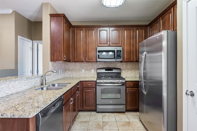 Kitchen with tasteful backsplash, light stone counters, stainless steel appliances, a sink, and light tile patterned flooring | Image 14