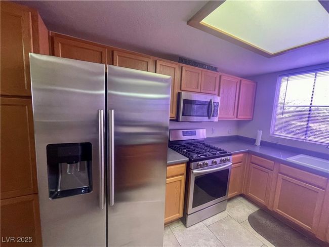 Kitchen with light tile patterned flooring, dark countertops, a sink, and appliances with stainless steel finishes | Image 7