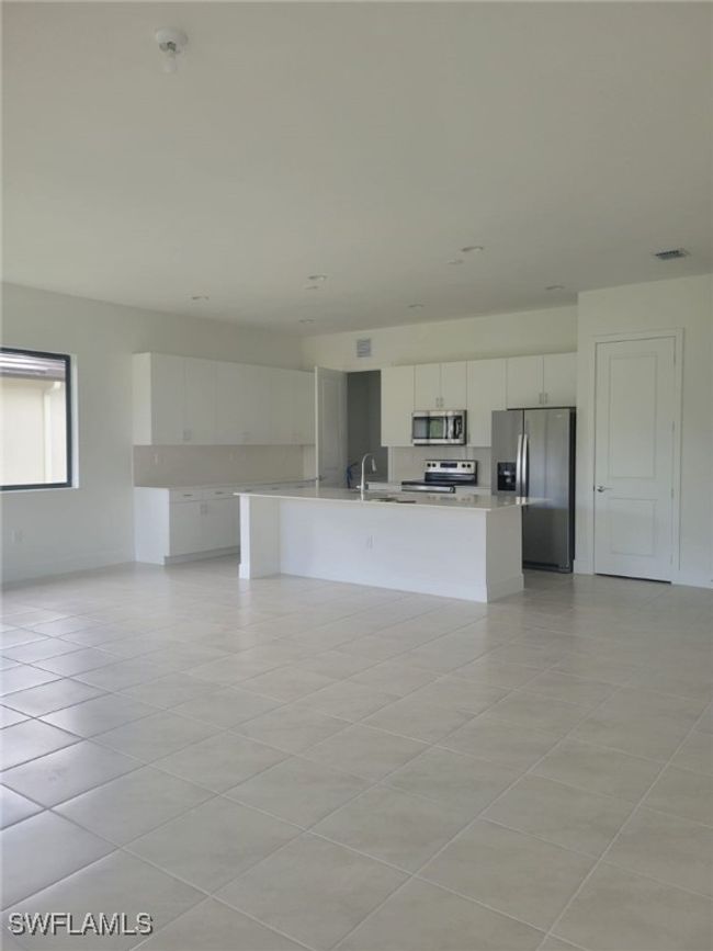Kitchen with stainless steel appliances, light countertops, white cabinetry, light tile patterned flooring, and a kitchen island with sink | Image 7