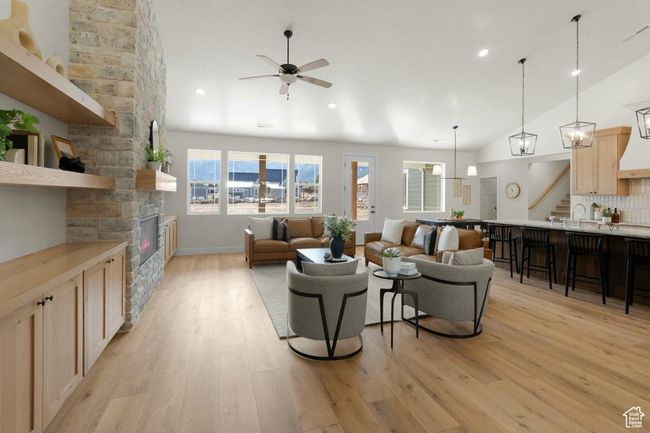 Living area featuring light wood finished floors, lofted ceiling, stairs, ceiling fan, and a stone fireplace | Image 4