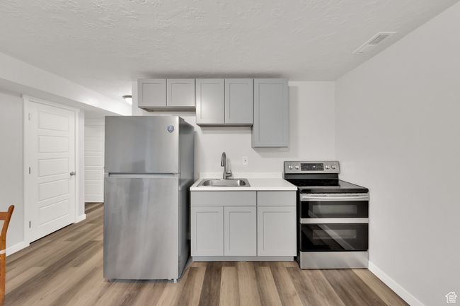 Kitchen featuring stainless steel appliances, gray cabinets, light wood-style floors, light countertops, and a textured ceiling | Image 29