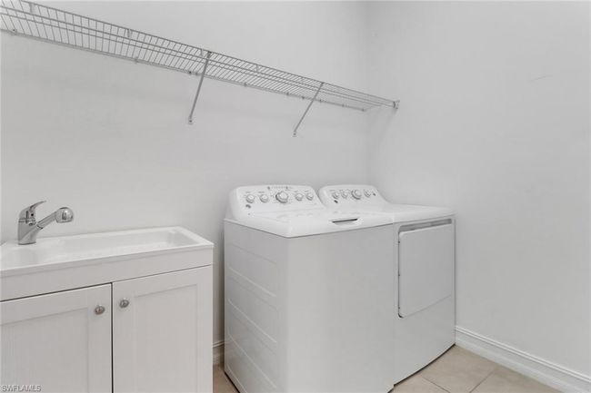 Laundry area featuring washing machine and dryer, light tile patterned flooring, cabinet space, and baseboards | Image 9