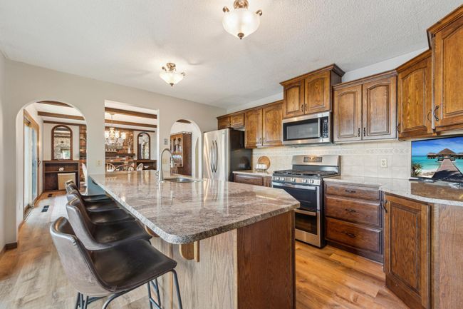 Beautifully designed kitchen with rich wood cabinetry, granite countertops, stainless steel appliances, and a large center island with bar seating. | Image 6