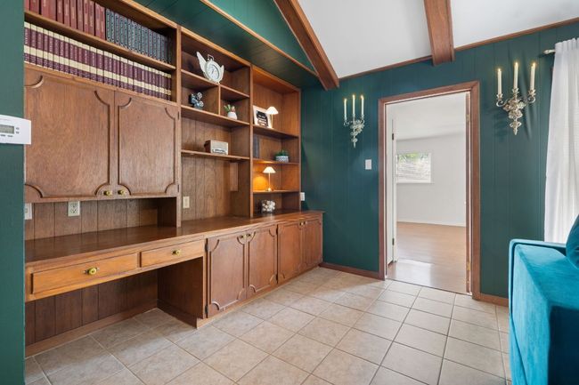 Office area with built-in bookshelves, light tile patterned floors, and wood panel walls. The door opens up to the primary bedroom. | Image 17