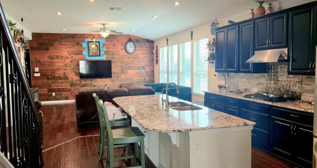Kitchen with ceiling fan, under cabinet range hood, dark wood finished floors, an island with sink, and gas cooktop | Image 12
