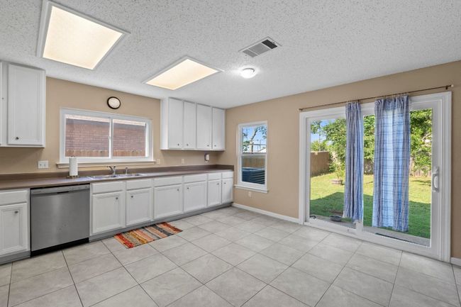 Kitchen with dishwasher, a sink, white cabinetry, a textured ceiling, and baseboards | Image 13