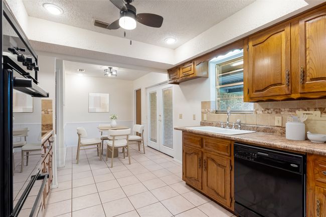 Kitchen with black appliances, a sink, brown cabinets, a textured ceiling, and decorative backsplash | Image 9