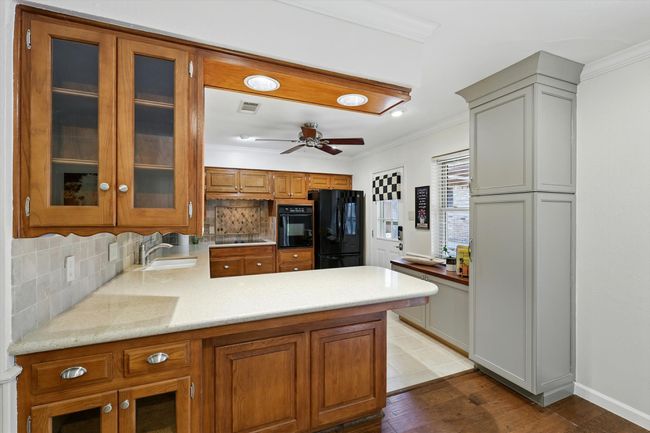Kitchen featuring black appliances, ornamental molding, a ceiling fan, decorative backsplash, and glass insert cabinets | Image 13