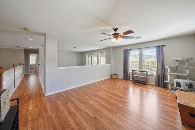 This spacious, bright room features hardwood flooring, a ceiling fan, and ample natural light from large windows. Perfect for a family gameroom, it offers a versatile layout with an open railing overlooking downstairs. | Image 23