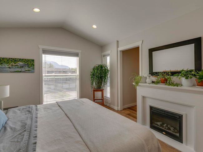 Bedroom with light wood finished floors, vaulted ceiling, a glass covered fireplace, baseboards, and recessed lighting | Image 21
