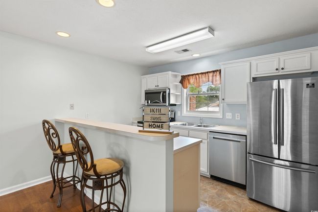 Kitchen featuring stainless steel appliances, a kitchen bar, light countertops, white cabinetry, and recessed lighting | Image 13