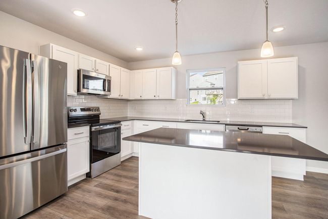 The kitchen features upgraded finishes, including quartz counters accented by tile backsplash. The large center island has an extended edge to accommodate barstools and there is pendant lighting above, making it an ideal place to prep or display food. The island can also be utilized as a study space, or a general gathering area. Full stainless steel appliance package included! | Image 4