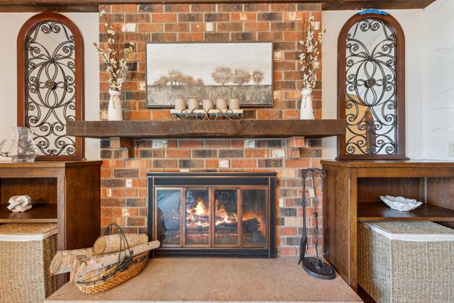 Beautiful brick surround fireplace with a rustic wood mantel, built-in shelving, and charming decorative ironwork—perfect for cozy evenings. | Image 13