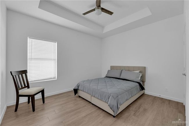 Bedroom with light wood-type flooring, a tray ceiling, and ceiling fan | Image 16