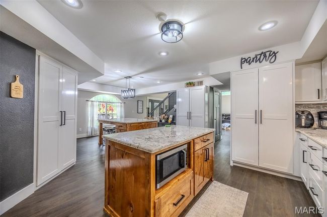 Kitchen with stainless steel microwave, a center island, white cabinetry, dark wood-type flooring, and recessed lighting | Image 25