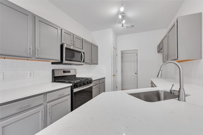 Kitchen featuring appliances with stainless steel finishes, gray cabinets, backsplash, and light stone countertops | Image 9