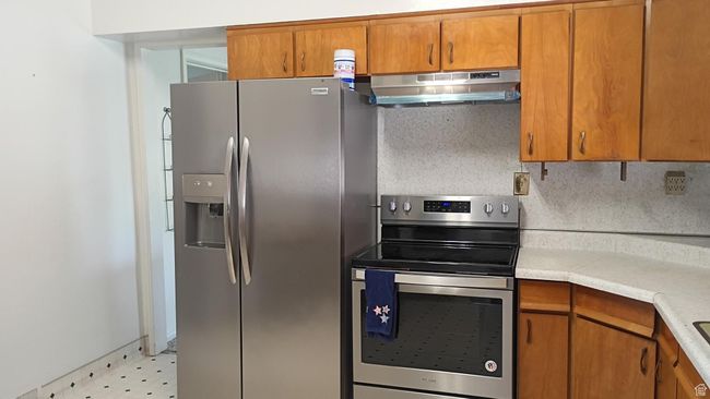 Kitchen featuring brown cabinetry, appliances with stainless steel finishes, light countertops, under cabinet range hood, and decorative backsplash | Image 17