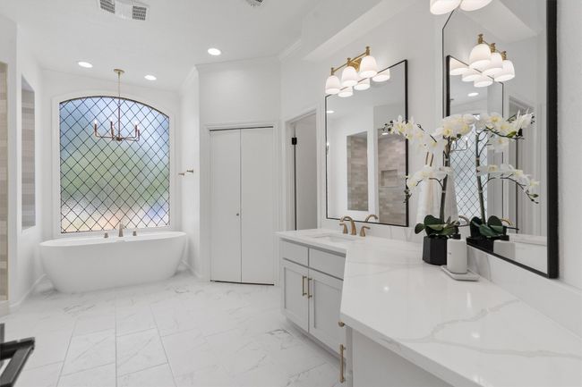 Full bathroom with a chandelier, marble look tiles, double vanity, a freestanding tub, and crown molding | Image 20