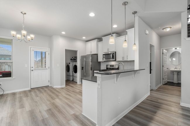Kitchen with appliances with stainless steel finishes, washer and dryer, dark countertops, light wood-type flooring, and recessed lighting | Image 8