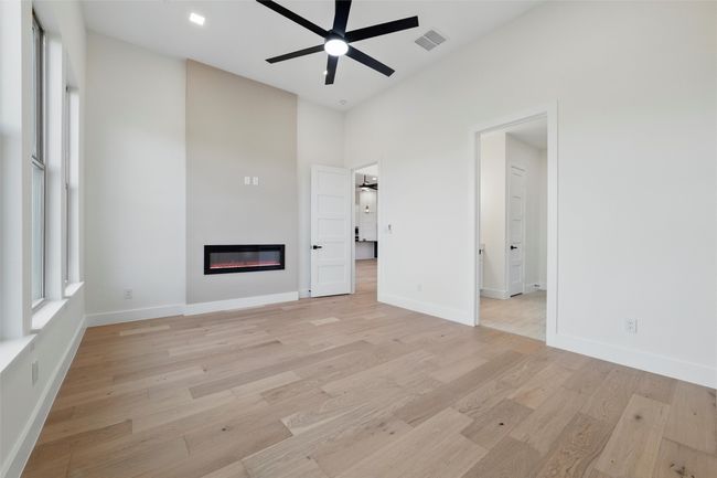 Unfurnished primary bedroom with ceiling fan, visible vents, a glass covered fireplace, and light wood finished floors | Image 30