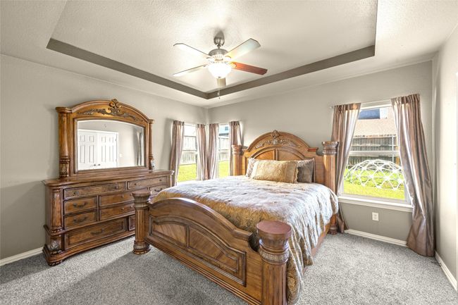 Master bedroom featuring a tray ceiling, baseboards, ceiling fan, and a textured ceiling | Image 14